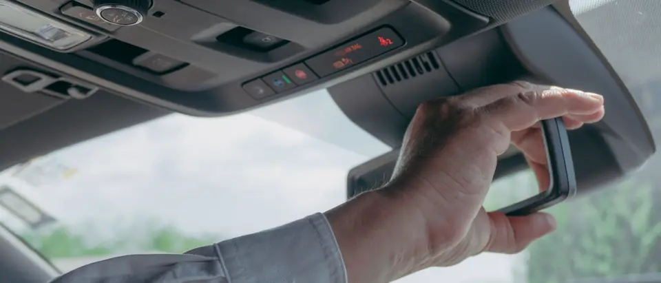 Hand adjusting the rear view mirror at the top of the windshield